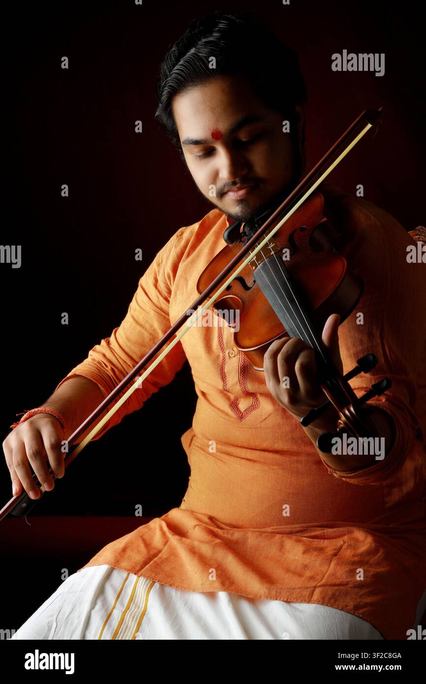 Ein Musiker in traditioneller Kleidung spielt mit ruhigem Ausdruck die Geige. Das warme Licht verleiht einen künstlerischen Touch und vermittelt Hingabe und Stockfoto