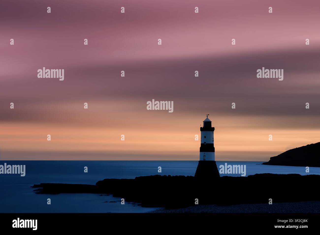 Penmon-Leuchtturm, Anglesey, Nordwales. Ruhiger Sonnenaufgang mit weichen Pastellfarben über dem Puffin Sound und einem ruhigen Irischen Meer. Stockfoto