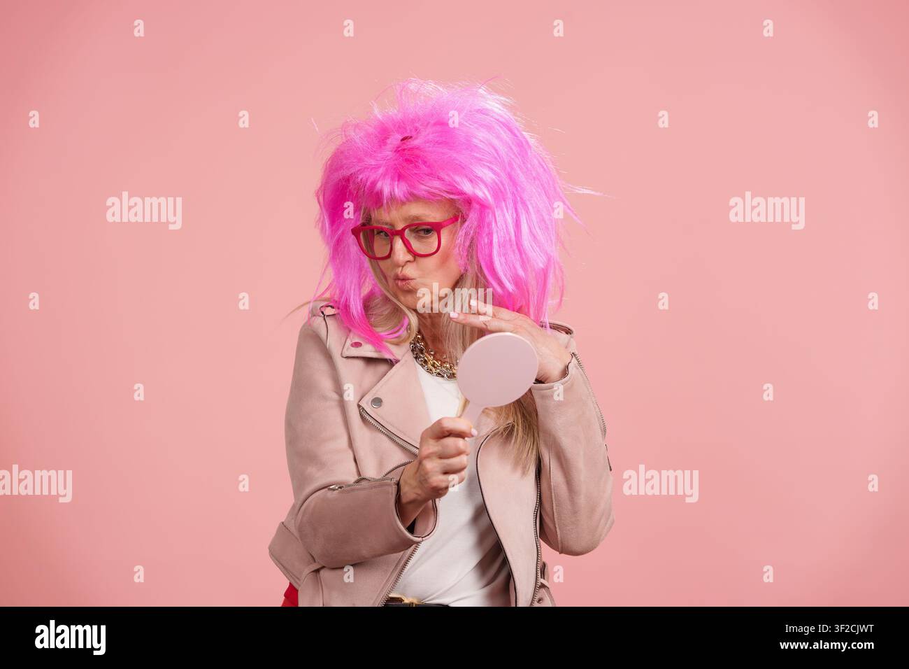 Reife Frau mit rosa Perücke überprüft ihr Aussehen im Spiegel Stockfoto