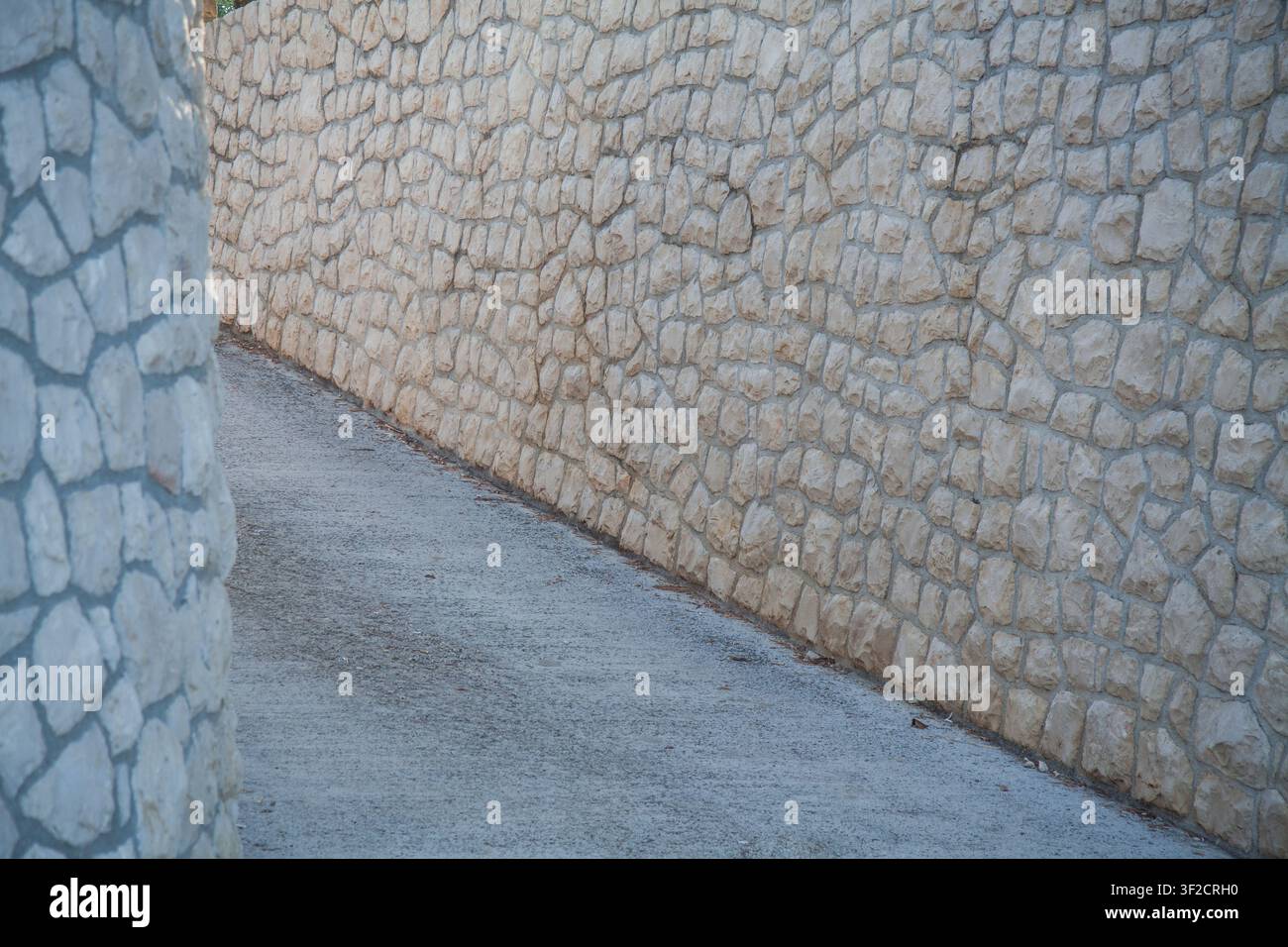 Nahaufnahme einer Steinmauer und eines angrenzenden Betonwegs, der eine Außentexturfläche mit Natursteinen in unregelmäßigen Mustern zeigt Stockfoto