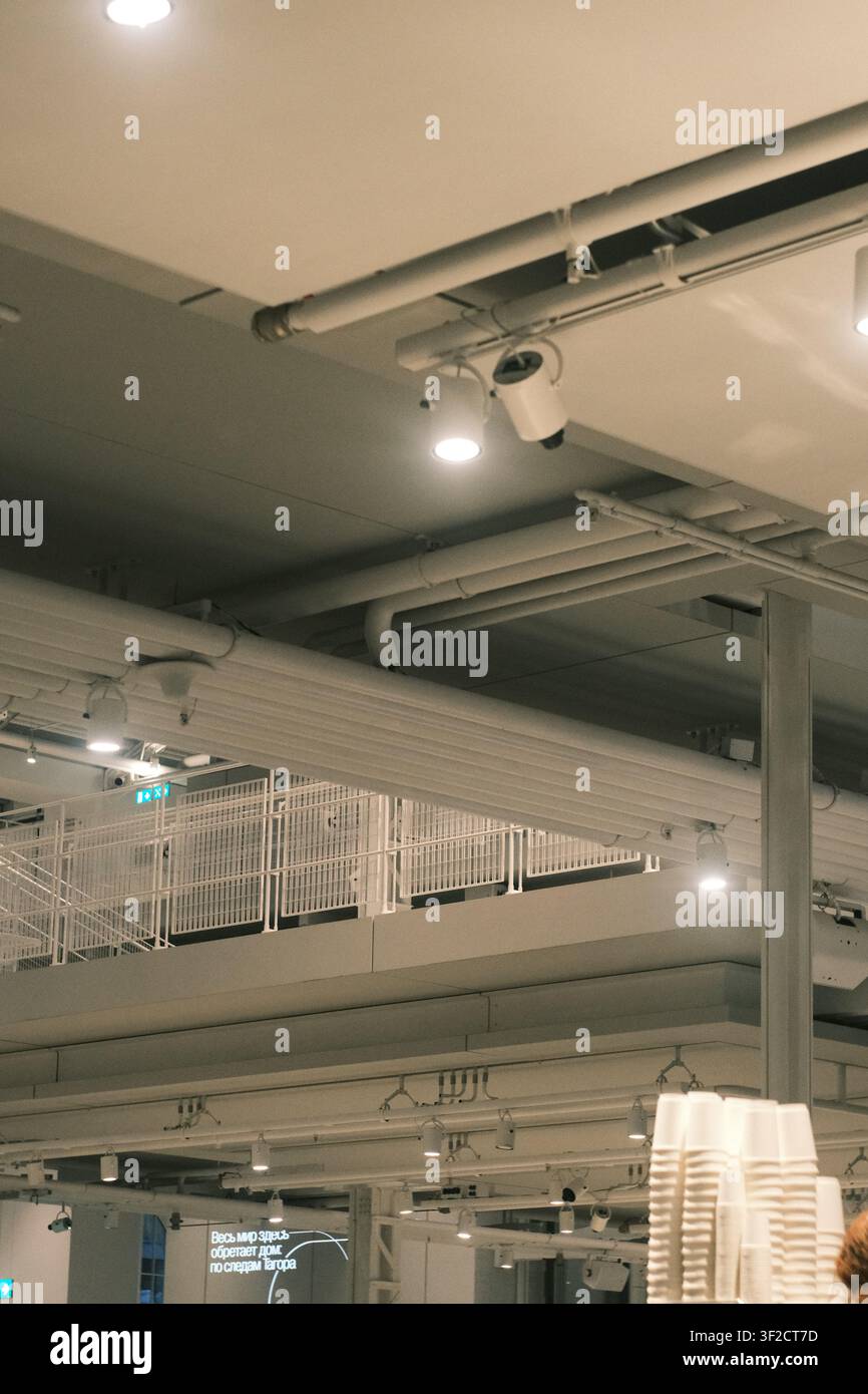 Moderne industrielle Innendeckendekoration mit freiliegenden Rohren, Lauflichtbeleuchtung und einer weißen Metall-Mezzanin-Struktur in einem gewerblichen Raum. Stockfoto