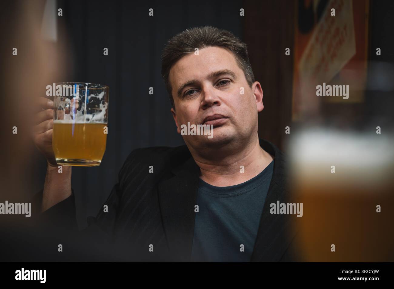 Freunde genießen Bier in einer Bar, einer hebt das Glas zum Anstoßen. Fröhlicher Trinkmoment. Stockfoto