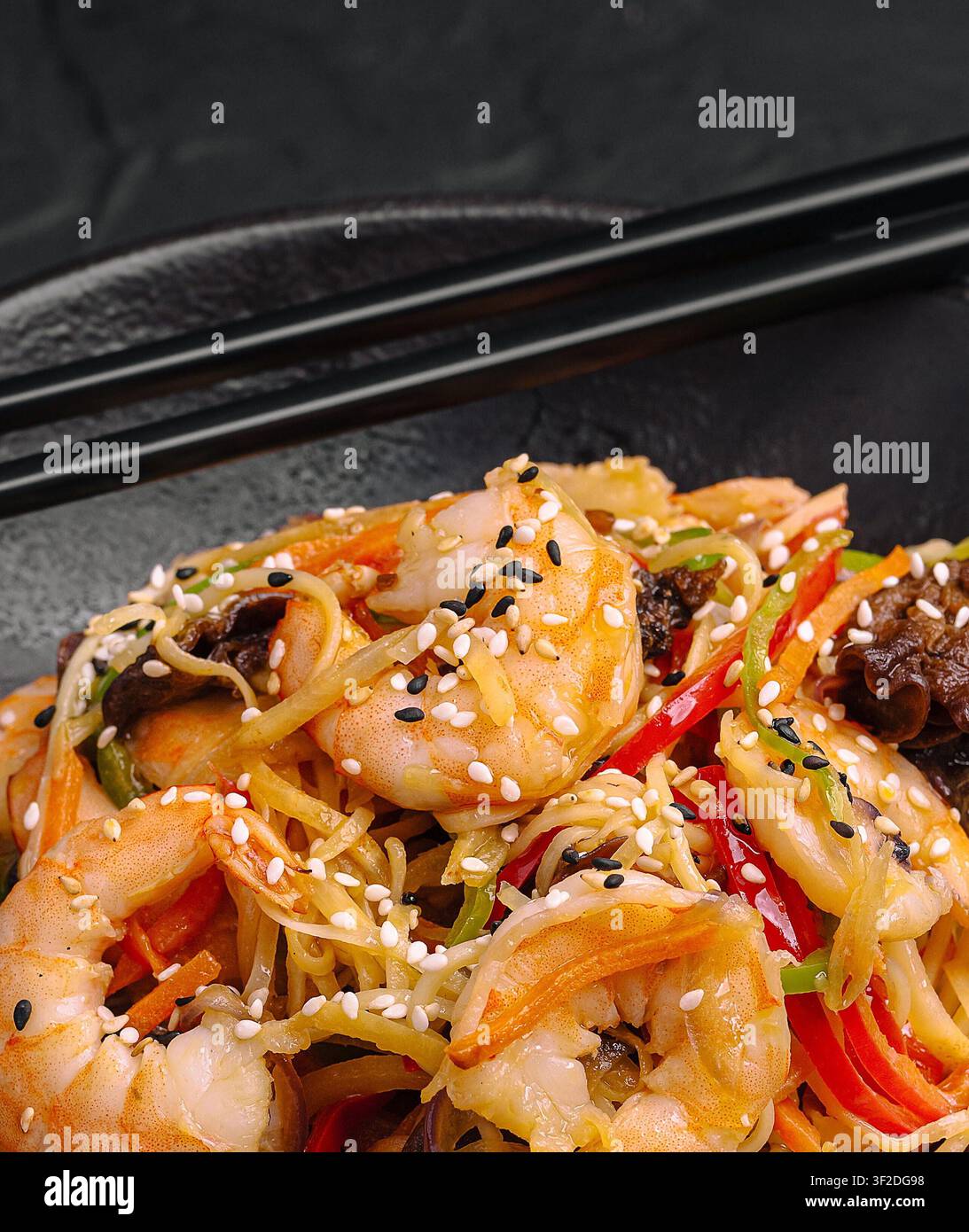 Asiatisches Chow-Mein-Stirfry mit Garnelen, Nudeln und bunten Gemüsen auf einem schwarzen Teller Stockfoto