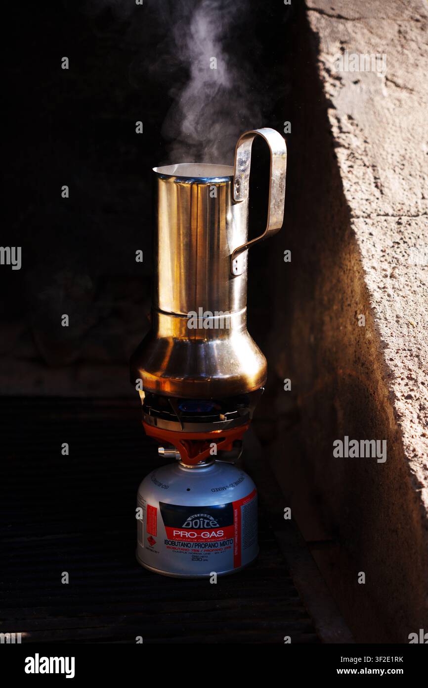 Kaffeemokkakanne mit Dampf auf einem Camping-Gaskocher im morgendlichen Sonnenlicht Stockfoto