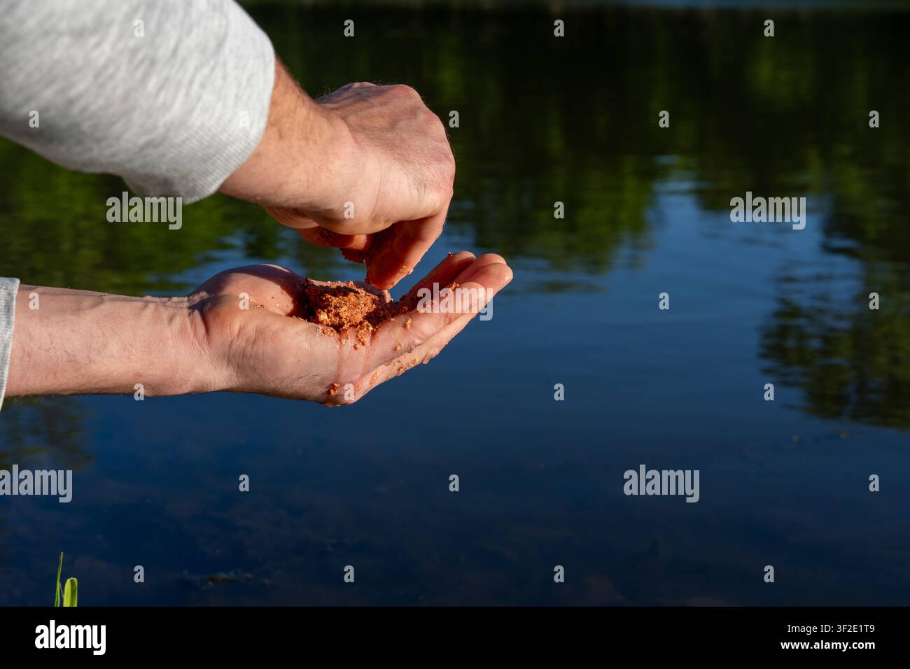 Eine Nahaufnahme aus der Ich-Perspektive einer Hand, die einen Ball Angelköder hält, bereit zum Angeln in einem Teich, wobei die Vorbereitungsphase des Angelns hervorgehoben wird Stockfoto