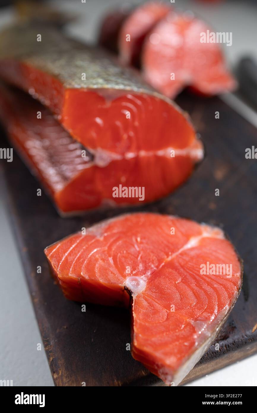 Geräucherte Sockeefischfilets liegen auf einer dunklen Holzplatte und zeigen tiefrotes Fleisch, eine glänzende Textur, einen silbernen Hautrand und feine Muskellinien, mit sanfter Hintergrundunschärfe und appetitlicher kulinarischer Präsentation Stockfoto