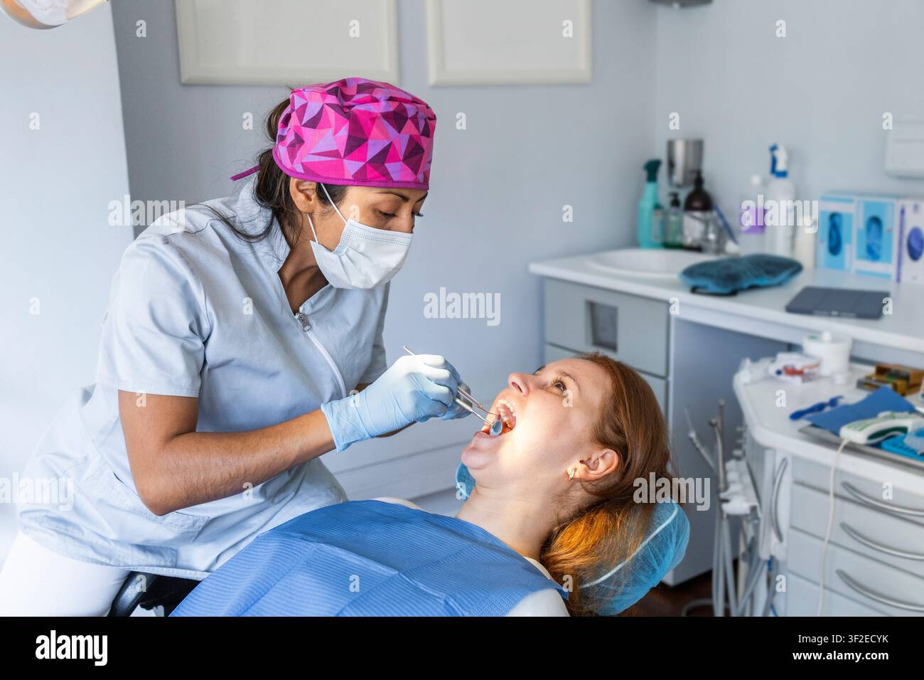 Ein Zahnarzt, der eine Maske und Handschuhe trägt, untersucht einen Patienten in einer modernen Zahnklinik. Der Patient ist entspannt, und die Klinikumgebung ist sauber und prof Stockfoto