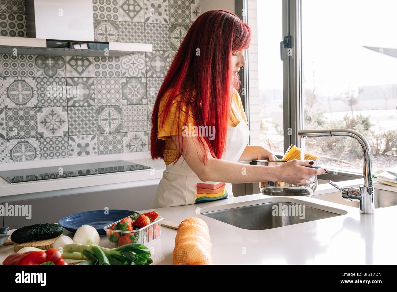 Junge Frau füllt einen Topf mit Wasser, um in ihrer Küchenstube Pasta zu kochen Stockfoto
