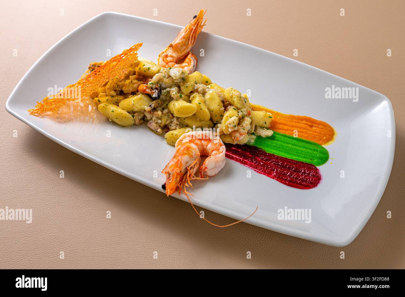 Gnocchi alla marinara mit Garnelen und Meeresfrüchten, elegant angerichtet mit bunten Gemüsesaucen in einer zeitgenössischen Fine-Dining-Präsentation. Stockfoto