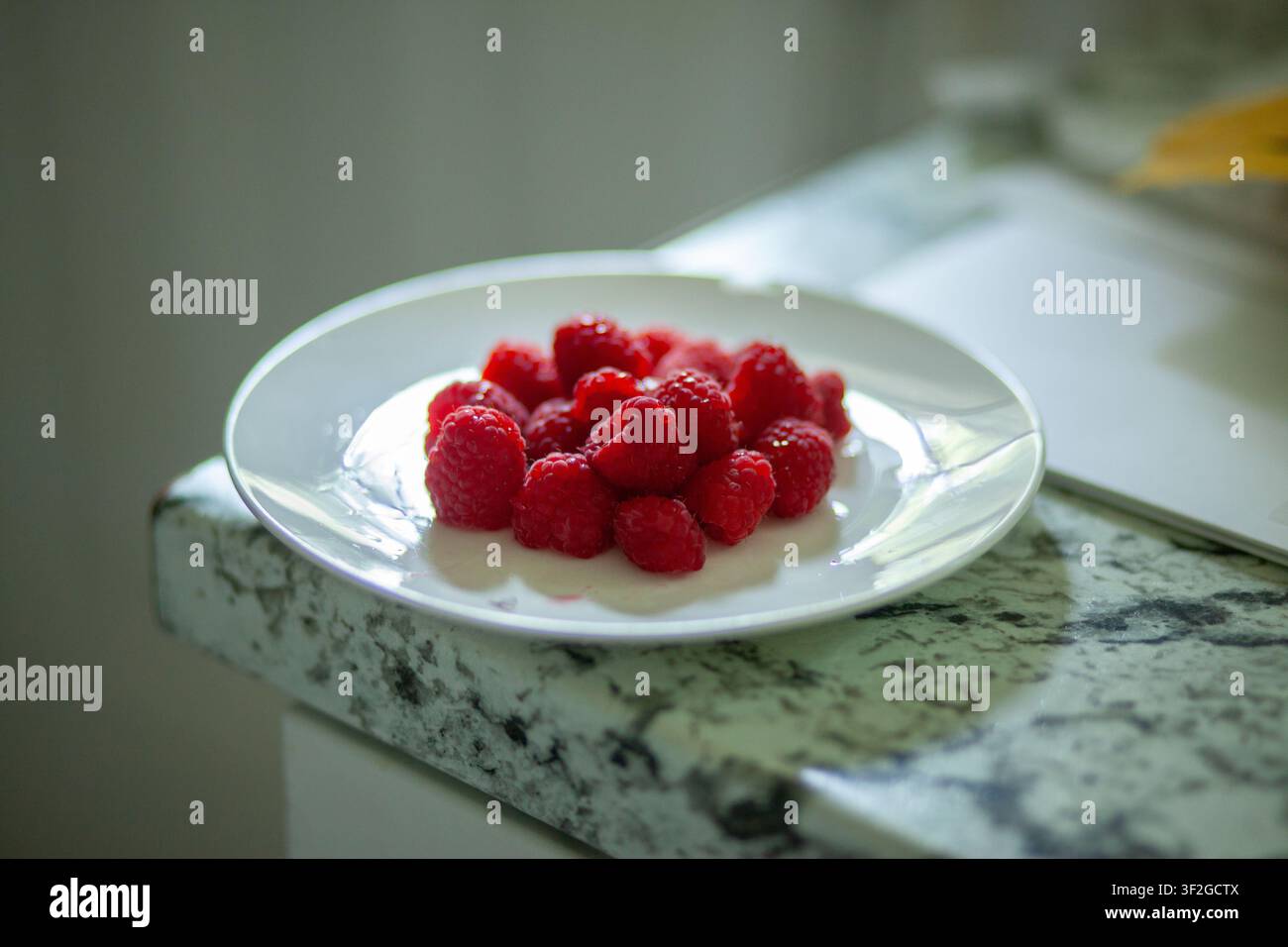 Weißer Teller mit Himbeeren am Rand einer Küchentheke Stockfoto