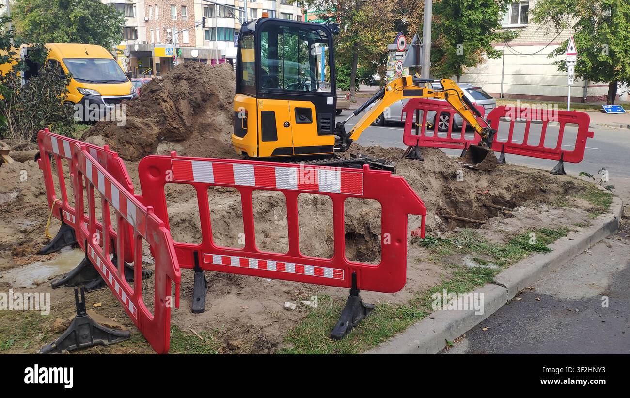 Kleiner gelber Bagger arbeitet an einer städtischen Straßenbaustelle Stockfoto
