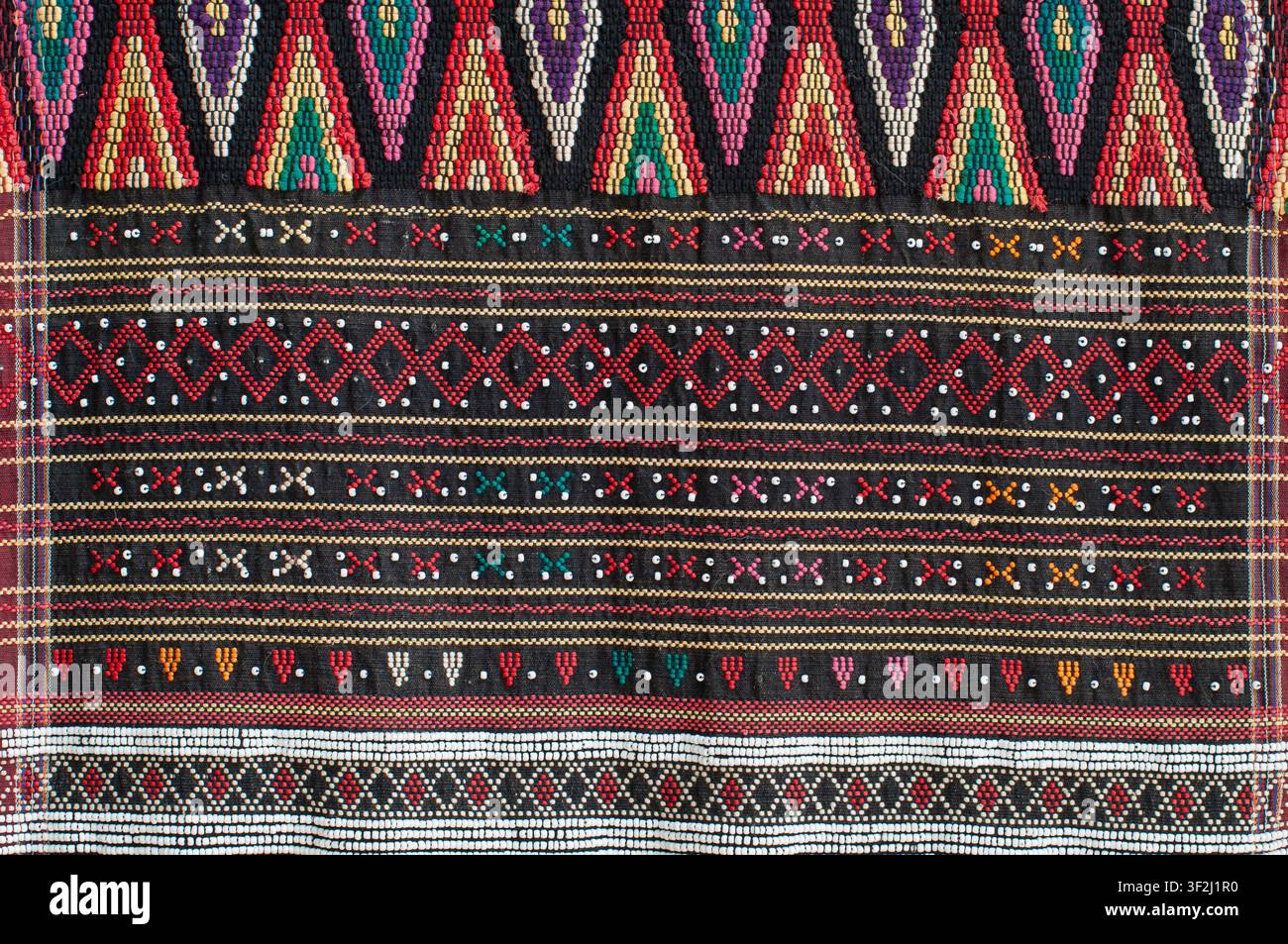 Detaillierte Ansicht eines farbenfrohen indonesischen Batak-Ulos-Textils mit geometrischen Stammesmustern, Perlenstickerei und traditionellem Weben auf dunklem Stoff. Stockfoto