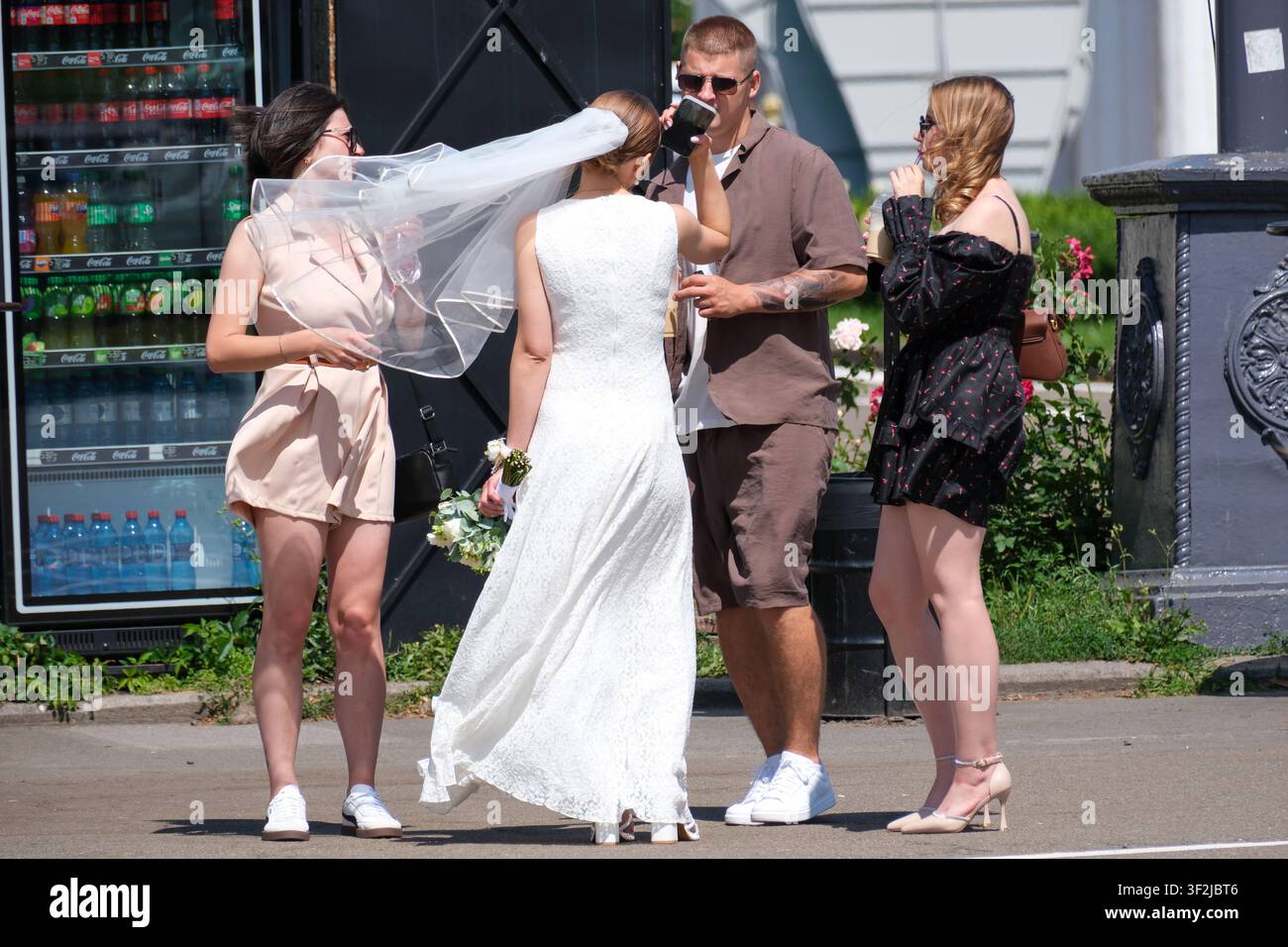 Kiew, Ukraine - 17. Juli 2026: Eine Braut in einem Hochzeitskleid und Schleier feiert mit Freunden während einer Hochzeitsfeier im Freien am VDNH (Expocente Stockfoto