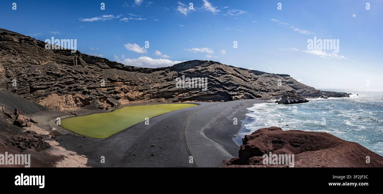 Lanzarotes einzigartige vulkanische Küstenlandschaft mit dem leuchtend grünen See, dem schwarzen Sandstrand und den Atlantikwellen Stockfoto