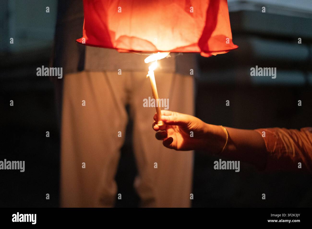 Nahaufnahme einer Person, die eine rote Papierhimmelslaterne mit einer Kerze anzündet, bevor sie während der Diwali- oder Makar-Sankranti-Feierlichkeiten in der Dämmerung freigelassen wird Stockfoto