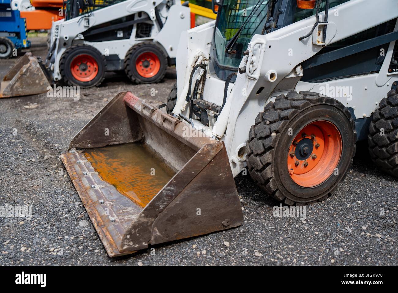 Ordentliche Aufstellung von kompakten Frontlader-Traktoren auf einem Kiesboden, die Konzepte von Maschinenmietlösungen und Baugeschäft abbilden Stockfoto