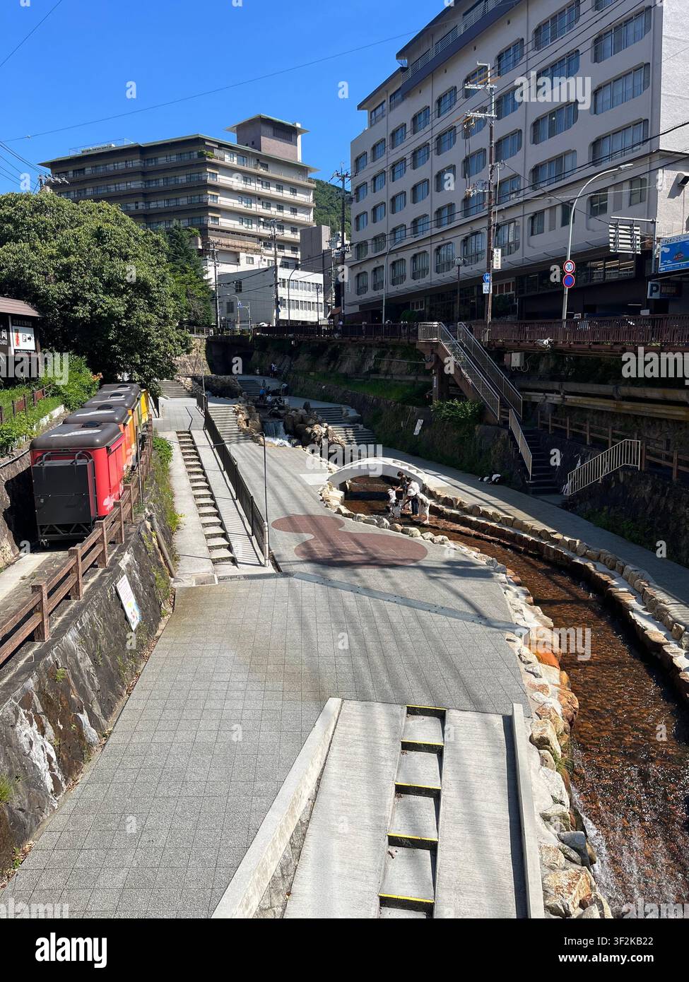 23. Juli 2023, Kobe, Japan – Urbane Kanal mit Steinufer, modernen Hotels und Straßeninfrastruktur in der Stadt Kobe an einem sonnigen Sommertag. - Smartphone-aufgenommenes Stockfoto