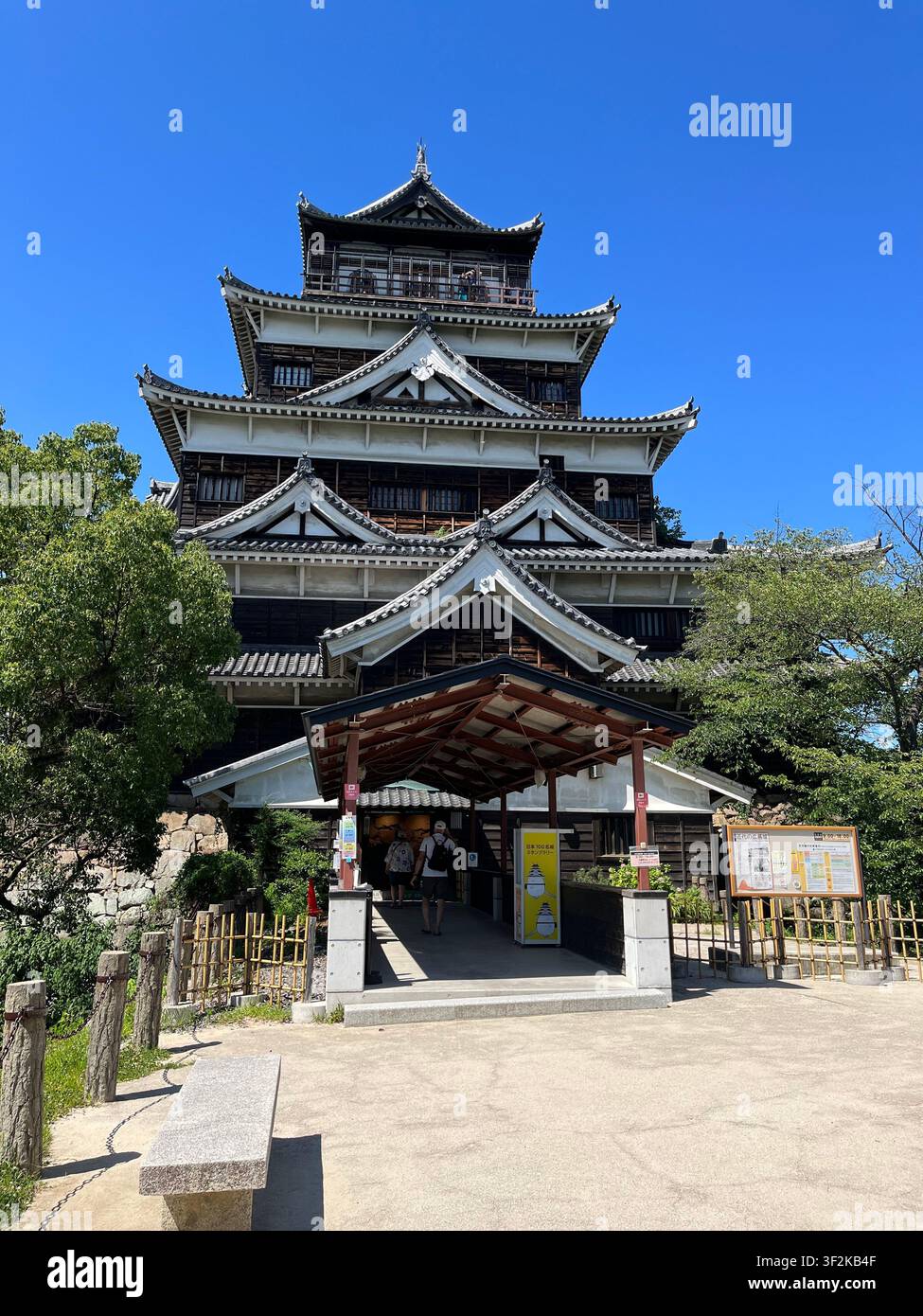25. Juli 2023, Kumamoto, Japan – Traditioneller japanischer Burgfried unter posterdbebenbedingter Restaurierung mit Gerüst, Besuchern und Informationsschildern an einem sonnigen Sommertag. - Smartphone-aufgenommenes Stockfoto