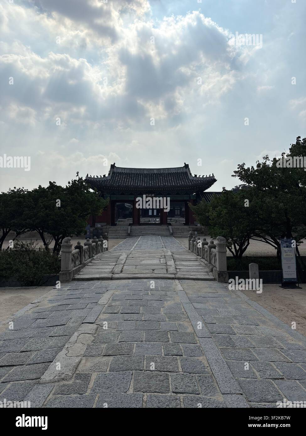 25. Juli 2025, Seoul, Südkorea – Steinpflasterhof am Gyeongbokgung-Palast mit traditionellem Hanok-Pavillon-Dach und dramatischen Sommerwolken. - Smartphone-aufgenommenes Stockfoto