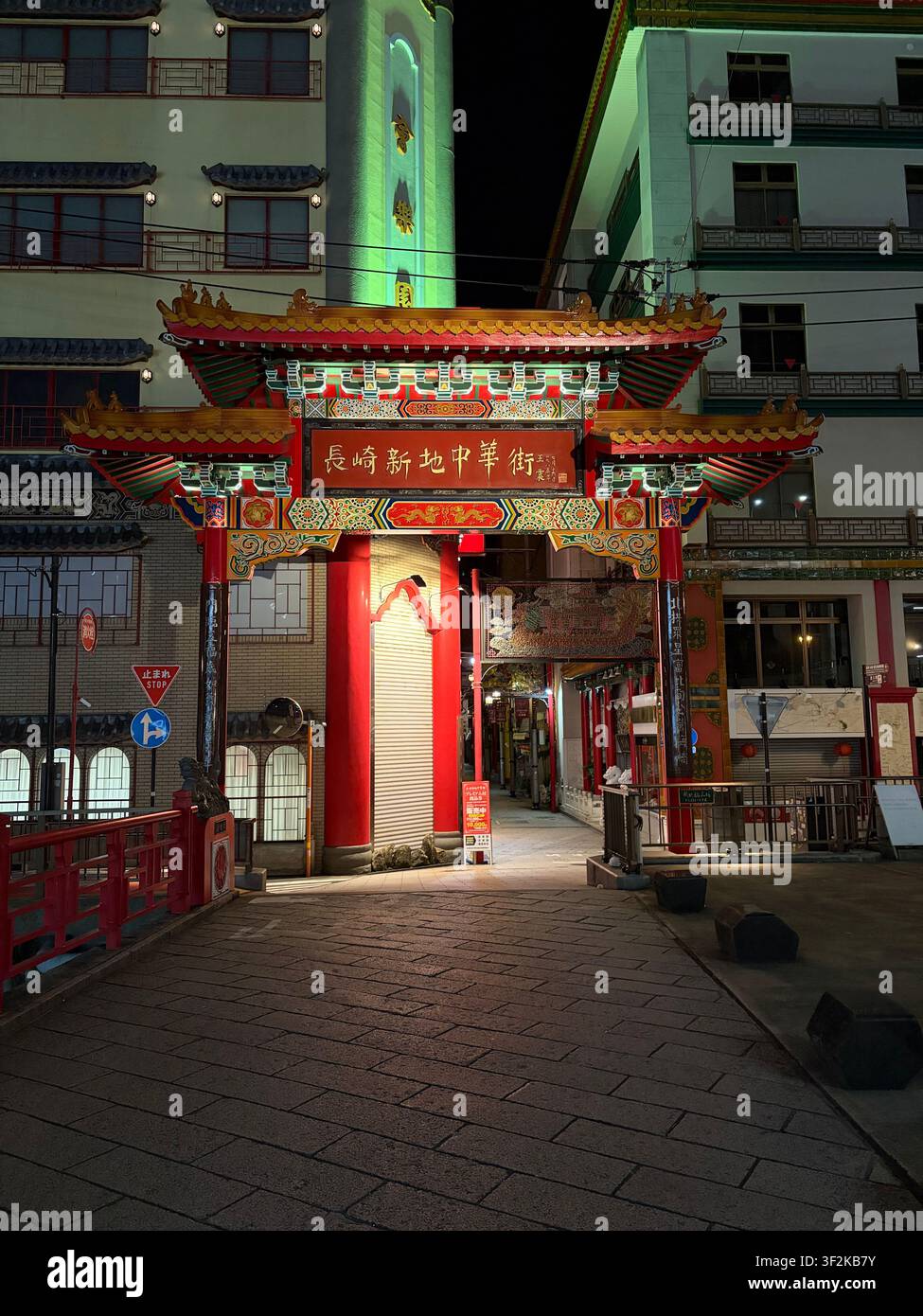 10. Oktober 2025, Nagasaki, Japan – Verziertes rotgoldenes Tor der Nagasaki Shinchi Chinatown bei Nacht beleuchtet, mit chinesischen Schriftzeichen und traditioneller Architektur. - Smartphone-aufgenommenes Stockfoto