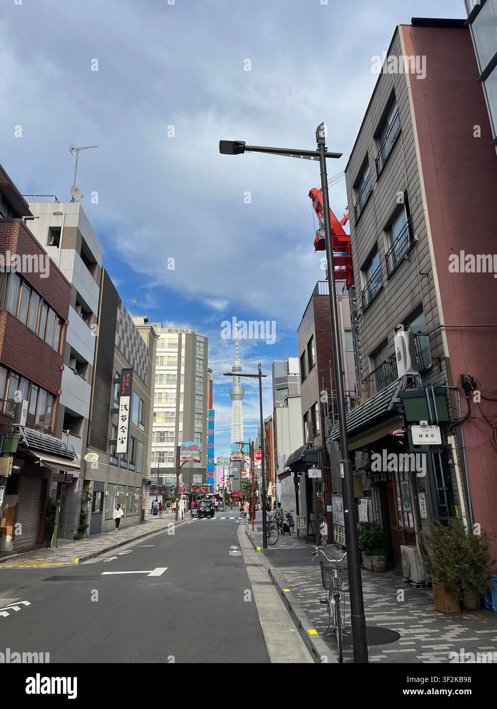 31. Juli 2023, Taito, Tokio, Japan – Urbane Straßenszene im Taito-Bezirk mit dem Tokyo Skytree-Turm, der über Geschäftshäusern aufragt und japanischen Ladenschildern. - Smartphone-aufgenommenes Stockfoto