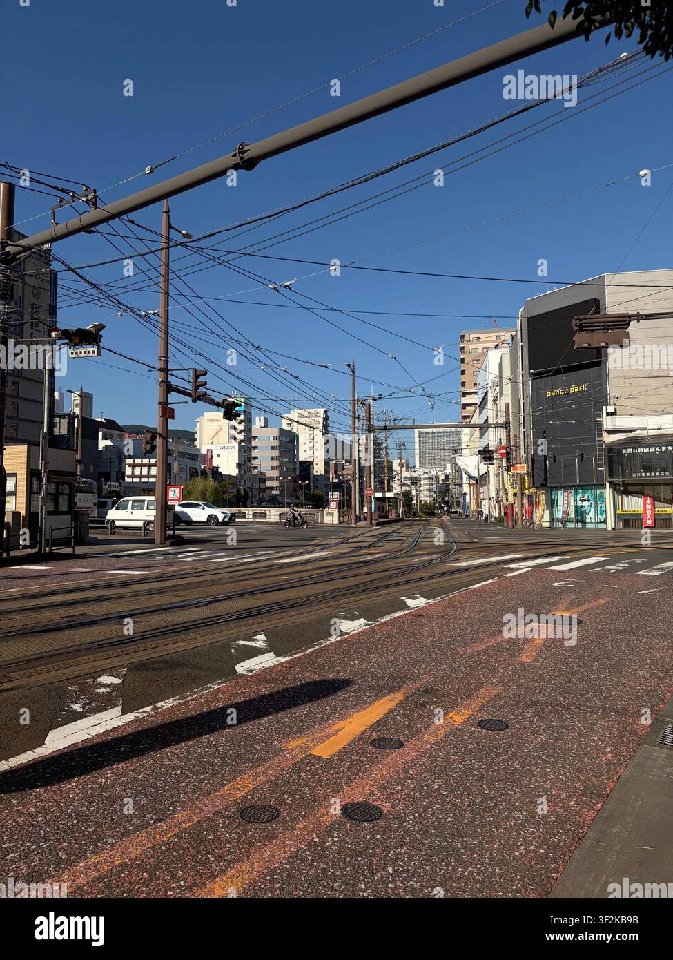 11. Oktober 2025, Nagasaki, Japan – Urbane Straßenbahnszene mit Oberleitungen, japanischen Ladenfronten, Straßenbahnschienen und Stadtgebäuden unter klarem blauem Himmel. - Smartphone-aufgenommenes Stockfoto