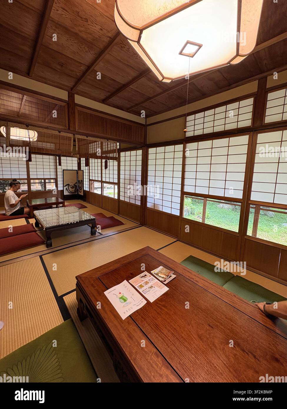 29. Juli 2025, Nara, Japan – Innenraum eines traditionellen japanischen Machiya oder Chaya mit Shoji-Bildschirmen, Tatami-Matten, hölzerner Gitterdecke und Gartenblick. - Smartphone-aufgenommenes Stockfoto