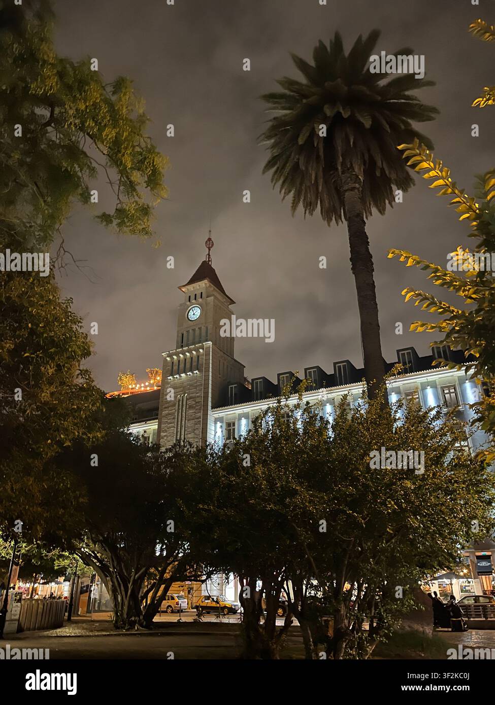 6. September 2023, [Stadt noch zu bestätigen] - Historischer Glockenturm bei Nacht beleuchtet, umgeben von Palmen und Nebel, Architektur im Kolonialstil mit warmen Straßenlaternen. - Smartphone-aufgenommenes Stockfoto