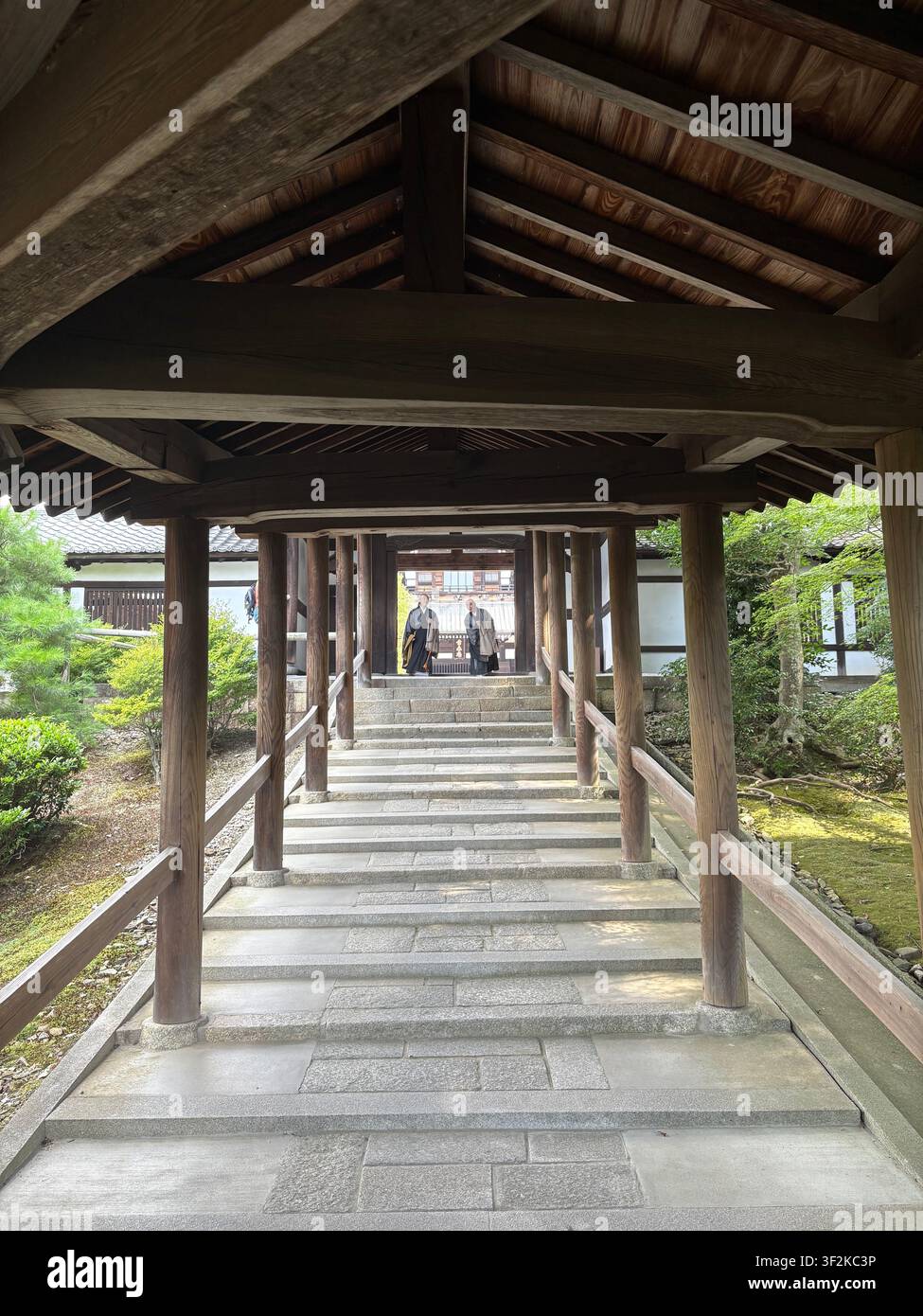 1. August 2025, Kyoto, Japan – Perspektivische Ansicht durch einen verwitterten Korridor aus Holztorii-Toren am Shinto-Schrein in Kyoto, im Hintergrund eine Person in traditioneller Kleidung sichtbar. - Smartphone-aufgenommenes Stockfoto