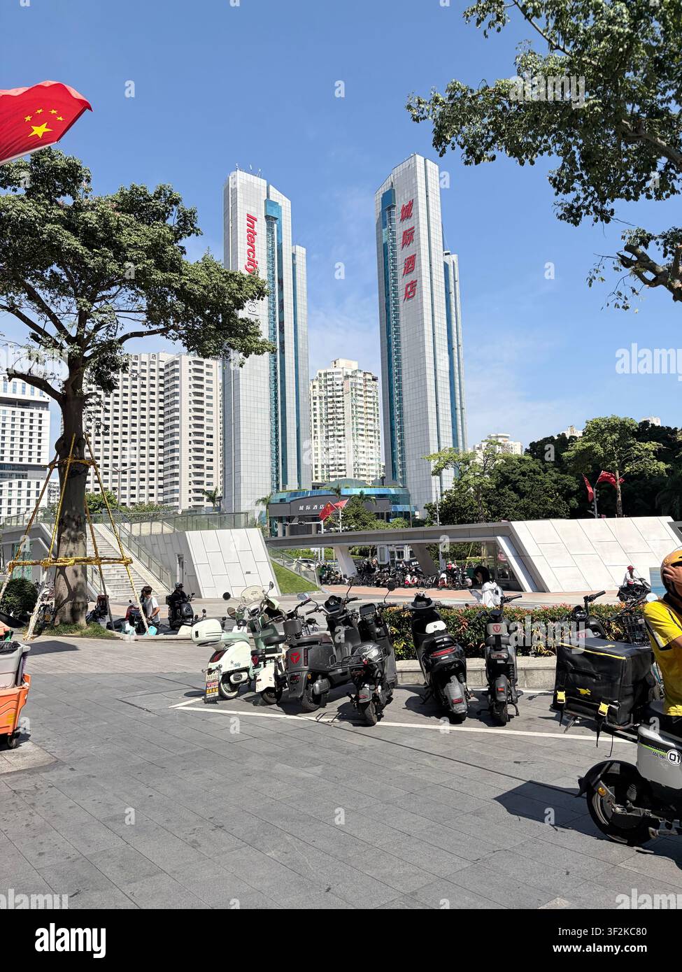 25. Oktober 2025, Shenzhen, China – Urbane Straßenszene im Futian-Bezirk mit den Zwillingstürmen des Intercity-Hotels, Elektroscootern und der chinesischen Nationalflagge. - Smartphone-aufgenommenes Stockfoto