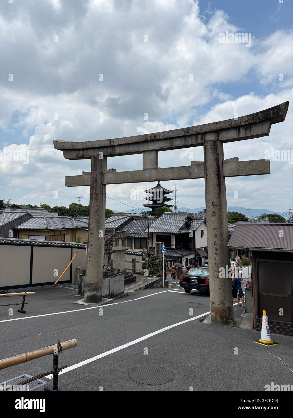 3. August 2025, Kyoto, Japan – Steinerne Torii-Tor mit japanischen Kanji-Inschriften, die ein traditionelles Pagoden-Dach entlang einer ruhigen städtischen Straße in Kyoto einrahmen. - Smartphone-aufgenommenes Stockfoto