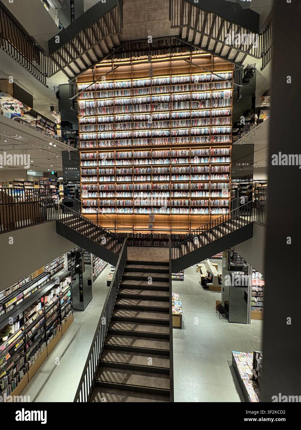 6. August 2025, Nagoya, Japan – Dramatischer Blick von unten auf eine mehrstöckige japanische Buchhandlung mit bodentiefen Manga- und Bücherregalen, Stahltreppen und warmer Beleuchtung. - Smartphone-aufgenommenes Stockfoto