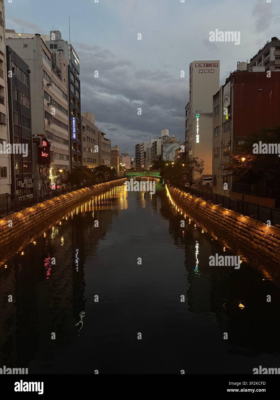 7. August 2025, Nagoya, Japan – Beleuchteter urbaner Boulevard in der Dämmerung mit leuchtenden Straßenlaternen, Neonreklamen und Stadtgebäuden, die sich im nassen Pflaster spiegeln. - Smartphone-aufgenommenes Stockfoto