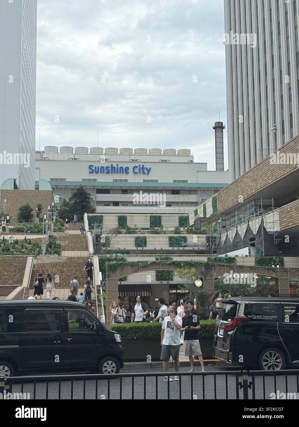 11. August 2025, Toshima, Tokio, Japan – Fassade des Sunshine-City-Komplexes mit Fußgängern und Fahrzeugen auf einer belebten Straße im Bezirk Ikebukuro, Tokio. - Smartphone-aufgenommenes Stockfoto