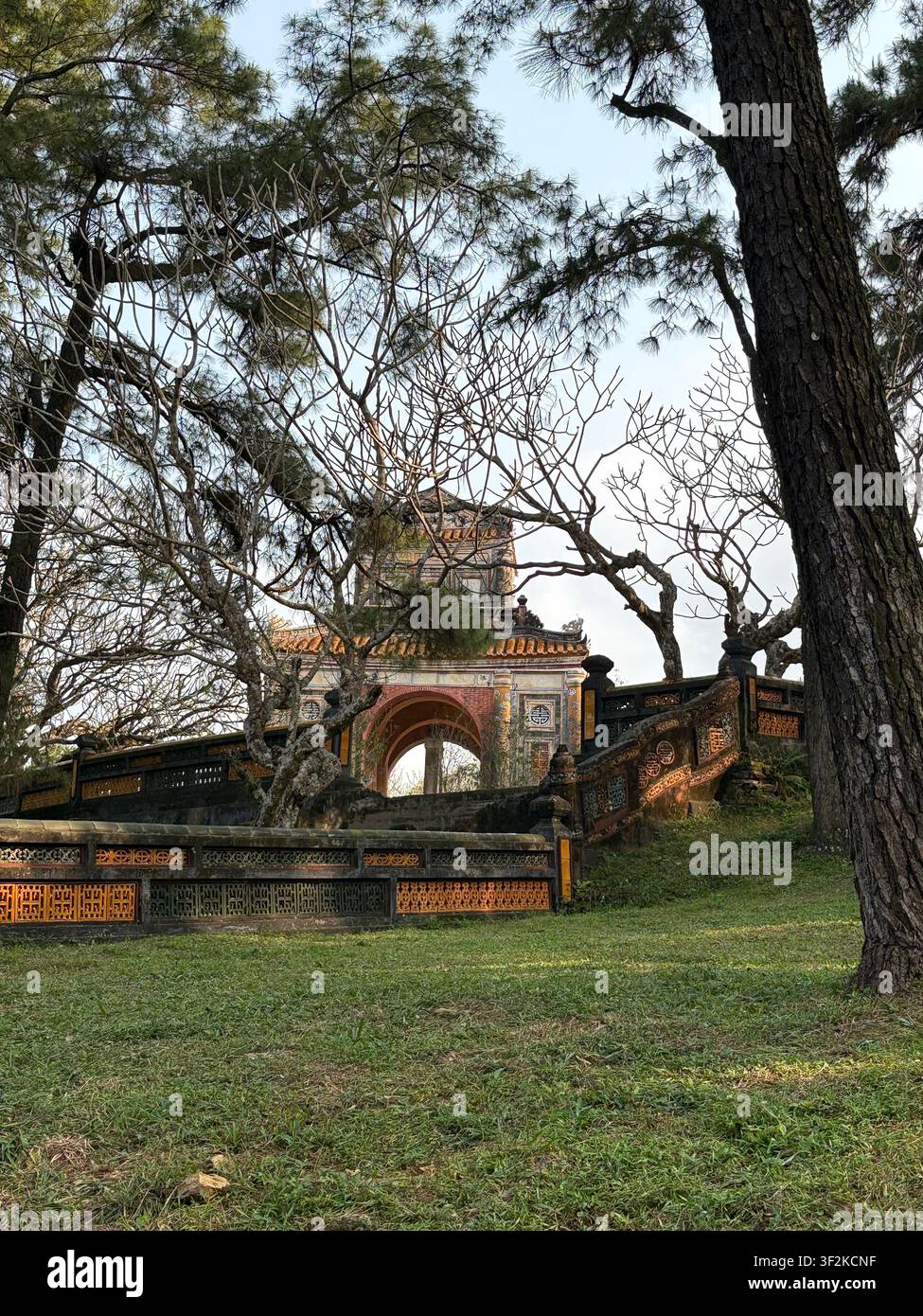 4. April 2025, Thá»§y XuÃ¢n, Hue, Vietnam - Verziertes imperiales Tor eines königlichen Grabes, eingerahmt von uralten Kiefern, das die traditionelle Architektur der vietnamesischen Nguyen-Dynastie präsentiert. - Smartphone-aufgenommenes Stockfoto