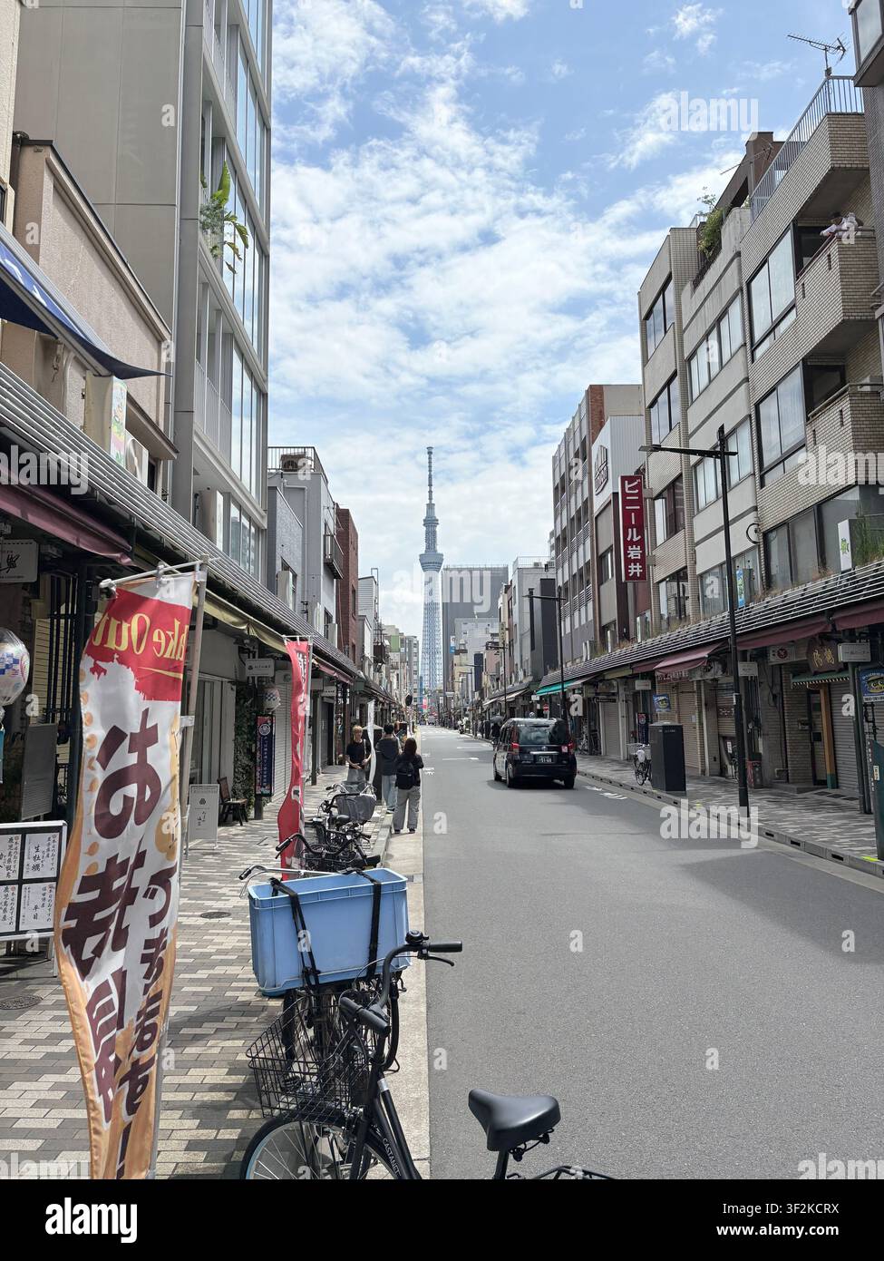 14. August 2025, Taito, Tokio, Japan – Straßenebene Ansicht einer lokalen Einkaufsstraße mit dem Tokyo Skytree im Hintergrund, japanische Banner und Fahrräder im Vordergrund. - Smartphone-aufgenommenes Stockfoto