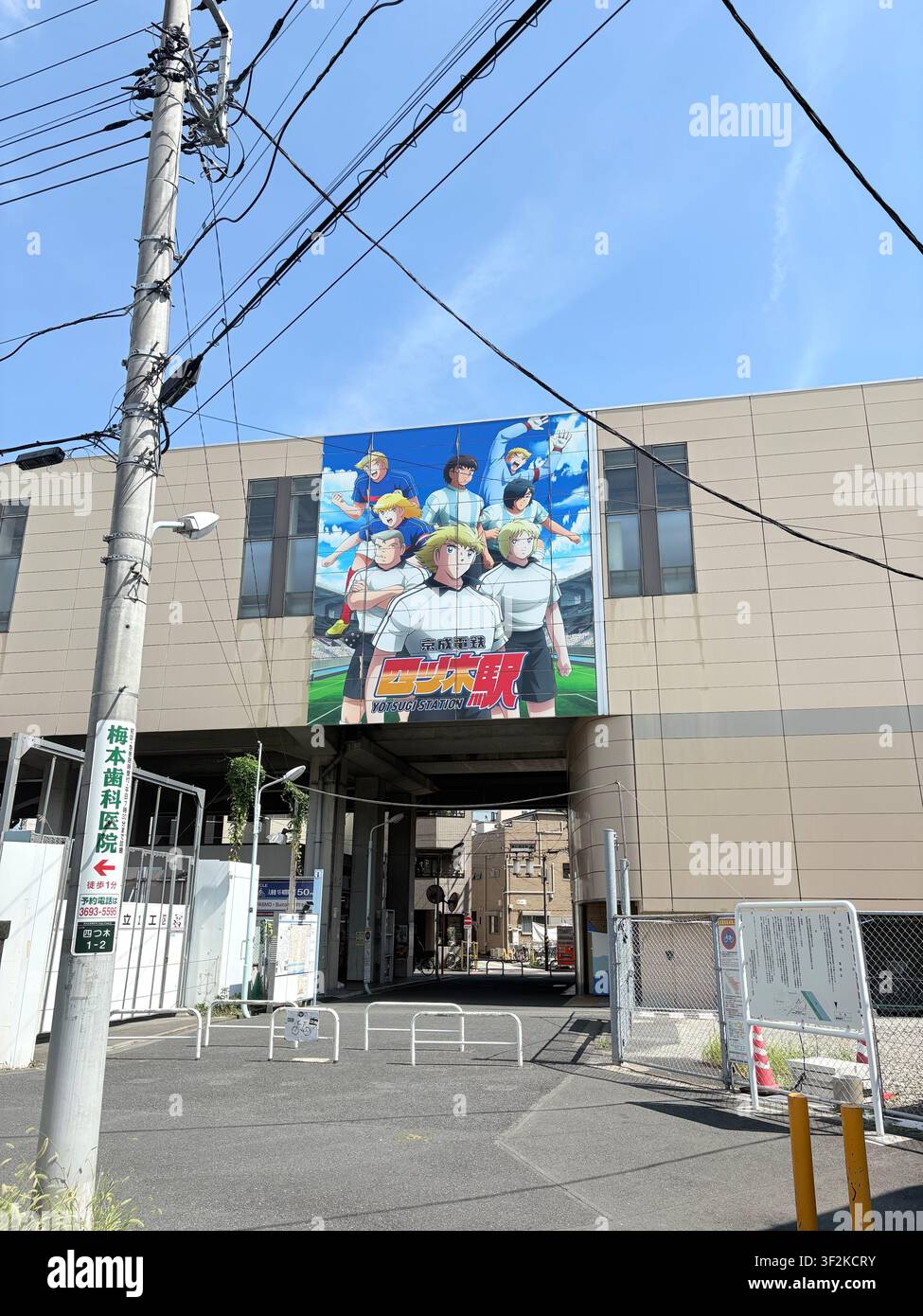 14. August 2025, Sumida, Tokio, Japan – Großes Anime-Manga-Murals an einer städtischen Gebäudefassade mit japanischen Straßenschildern und Stromleitungen im Vordergrund. - Smartphone-aufgenommenes Stockfoto