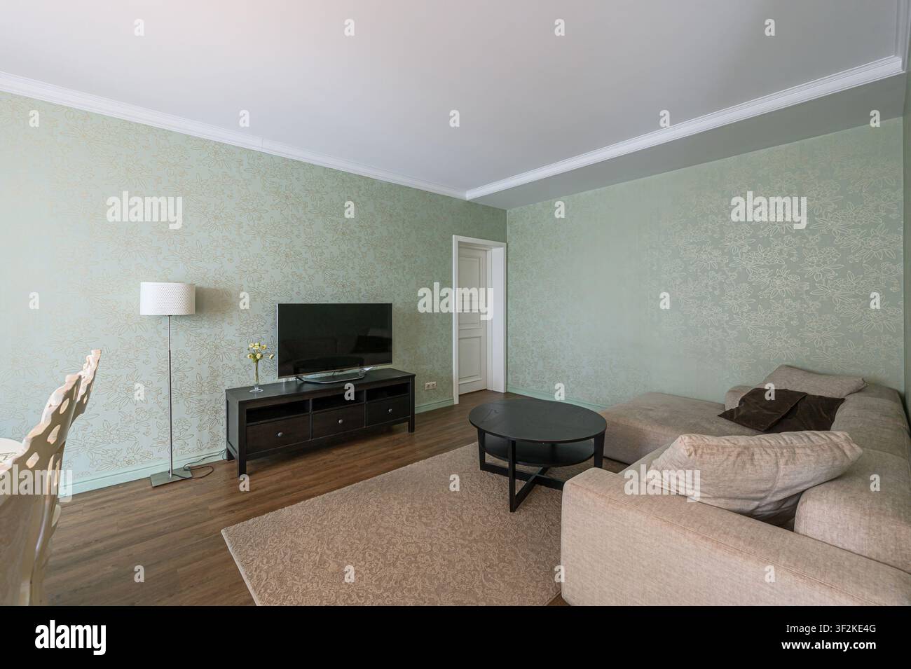 Gemütliches Wohnzimmer mit gemusterten Wänden, Fernseher, Sofa, Teppich und rundem Tisch. Eine Lampe sorgt für sanfte Beleuchtung Stockfoto