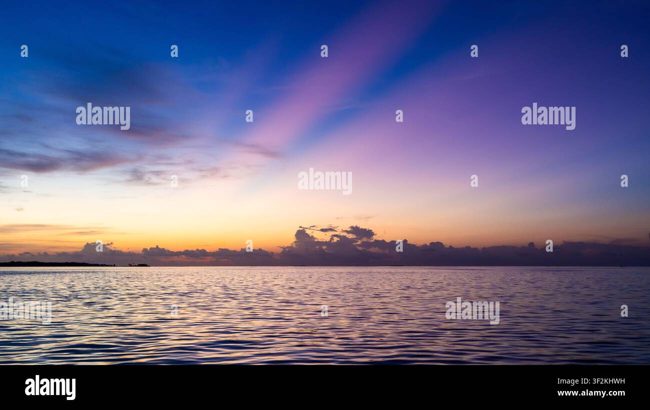 Farbenfroher Sonnenuntergang über dem ruhigen Indischen Ozean in der Nähe von Maamigili Island, Malediven, mit lila Wolken, die sich über dem ruhigen Wasser spiegeln. Stockfoto