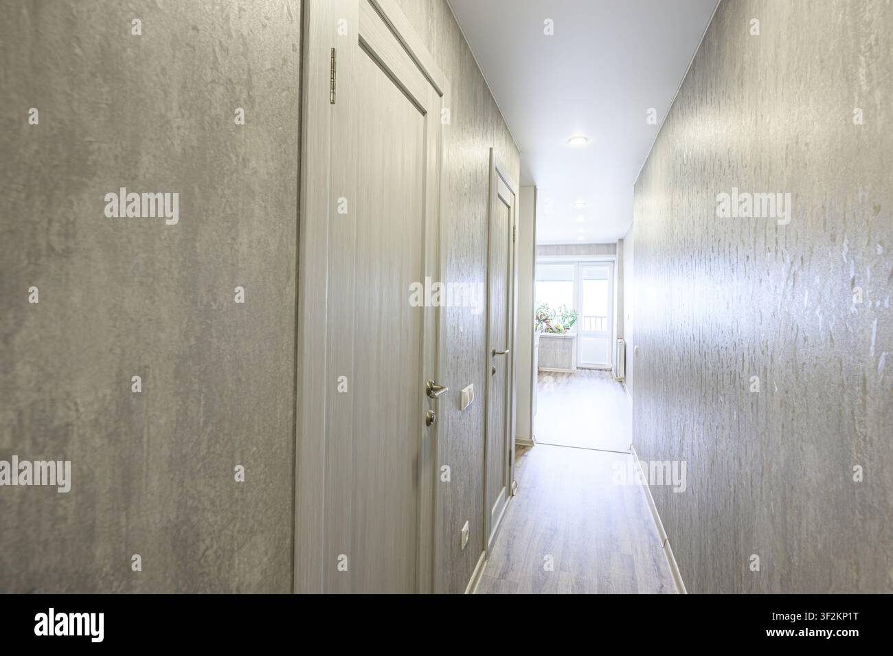 Türen reihen sich auf einer Seite an, führen zu einem hellen Ende mit einer Tür zu einem Balkon Stockfoto