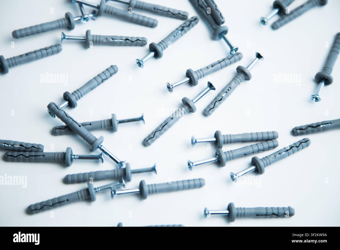 Viele graue Plastikdübel mit verschraubten Schrauben liegen chaotisch auf einem weißen Hintergrund verstreut Stockfoto