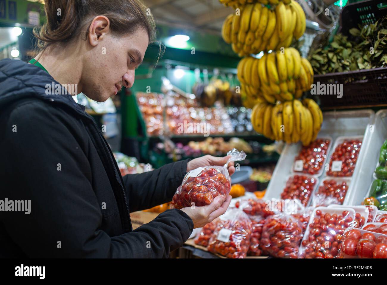 Kunde inspiziert und wählt frische Kirschtomaten auf einem öffentlichen Markt, wählt Produkte an einem Marktstand aus Stockfoto