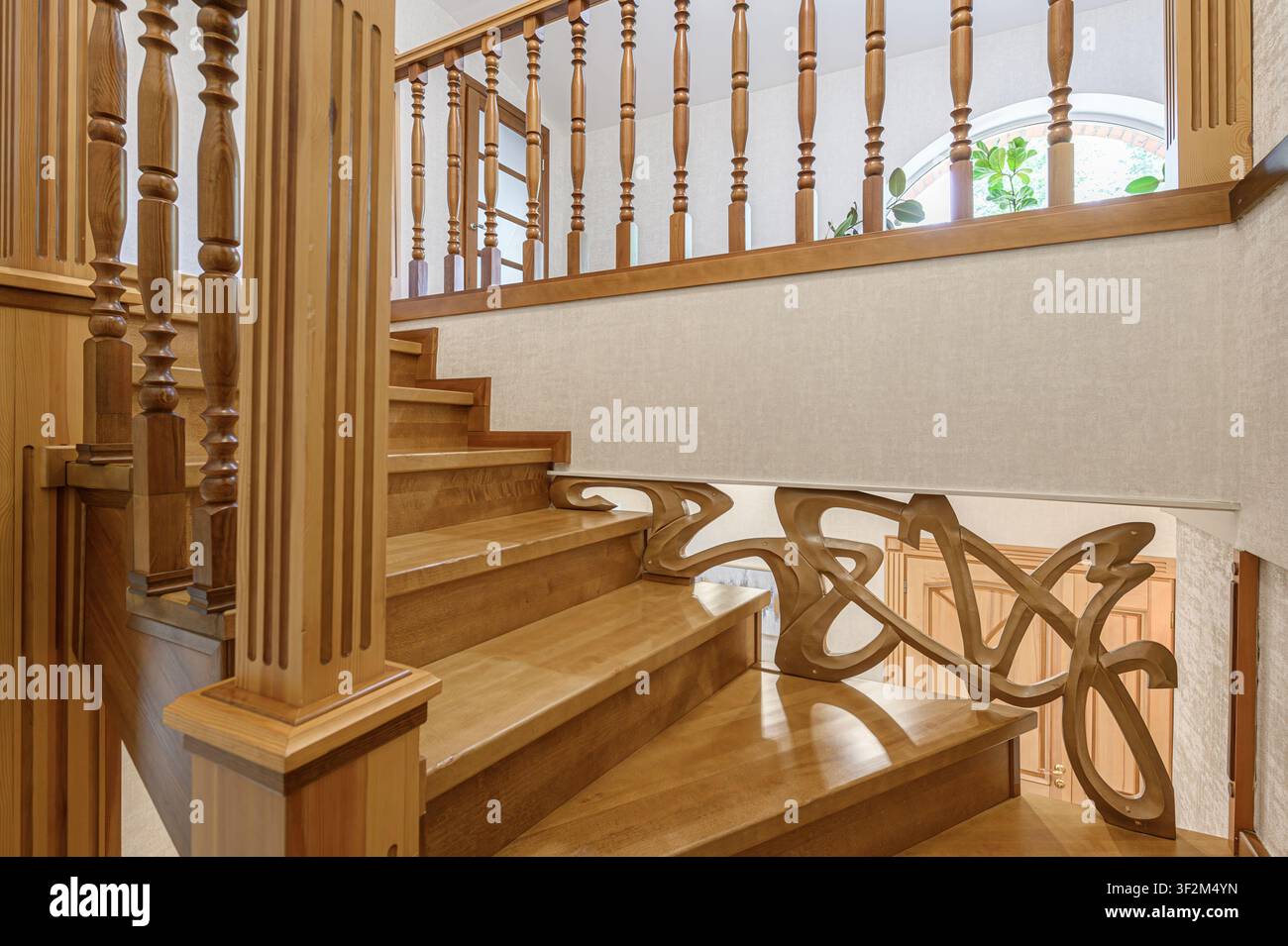 Holztreppe mit kunstvollen Geländern. Warme Beleuchtung, natürliche Holzoptik. Elegantes Wohninterieur-Detail Stockfoto