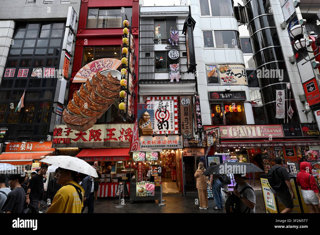 Besucher erkunden das lebhafte Dotonbori-Viertel in Osaka, Japan, vorbei an Restaurants, Arkaden und ikonischen Läden, die mit überdimensionalen Essensdiolen geschmückt sind Stockfoto