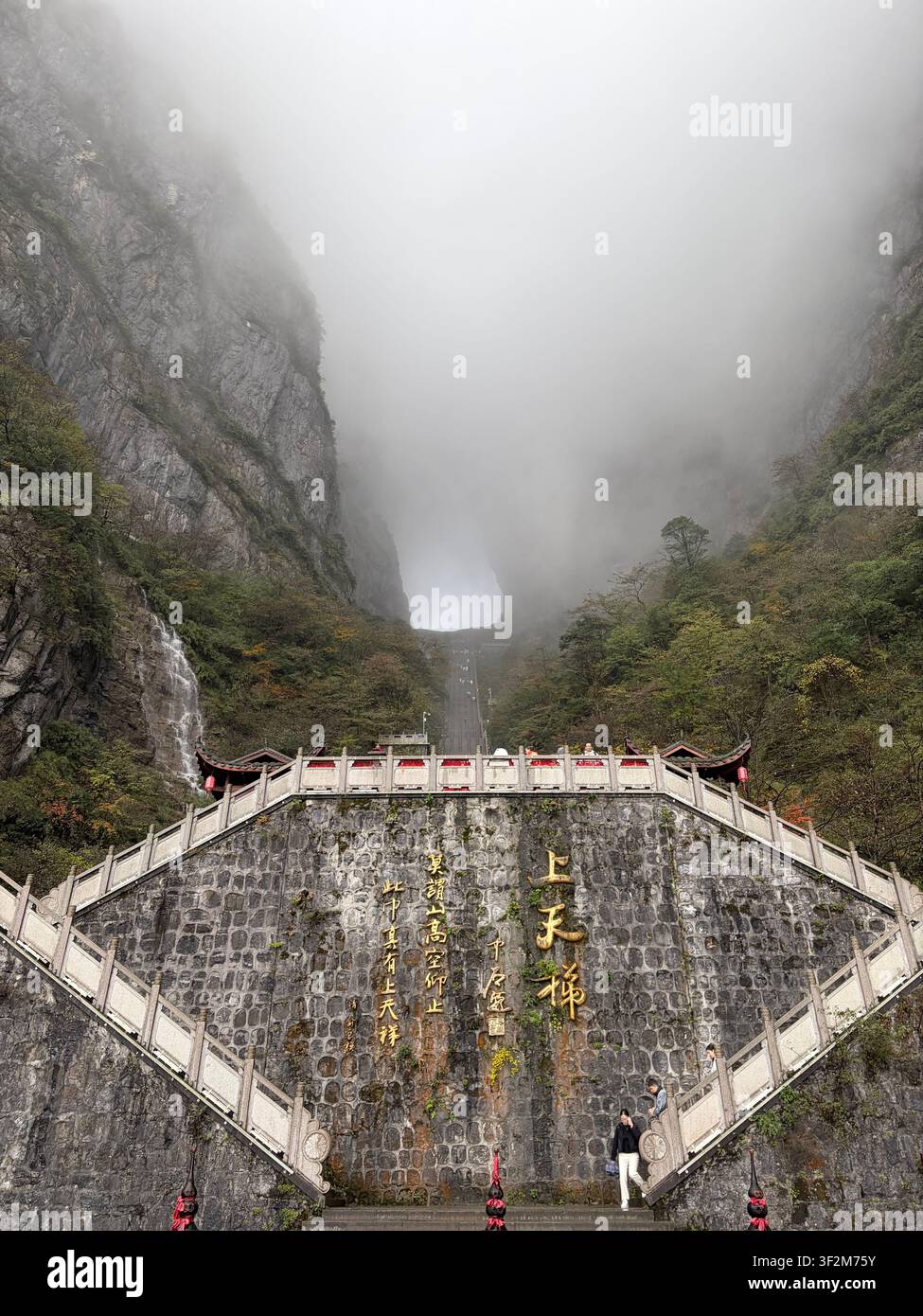 3. November 2025, Zhangjiajie, China – Steintor mit goldenen chinesischen Inschriften am Tianmen-Berg, umhüllt von dramatischem Nebel, Yongding-Distrikt. - Smartphone-aufgenommenes Stockfoto