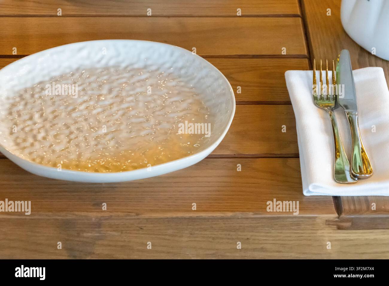Leere keramische Restaurantplatte auf Holztablett mit gefalteter Serviette und Besteck, vorbereitet für einen eleganten Essensservice. Stockfoto