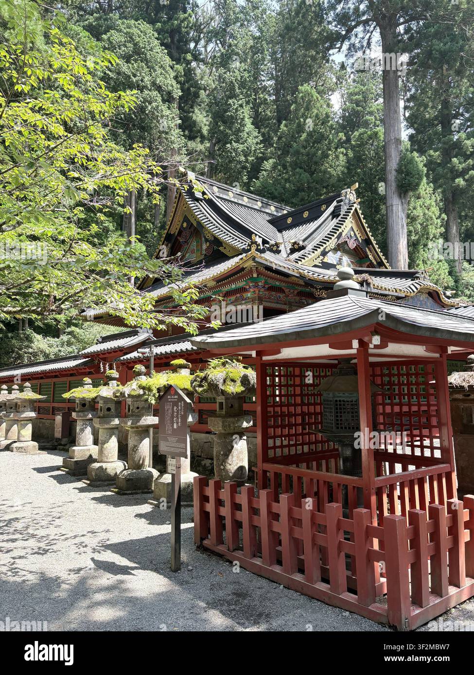 17. August 2025, NikkÅ, Japan – Verziertes schwarz-goldenes Pagoden-Dach und ein roter Tor mit moosbewachsenen Steinlaternen im UNESCO-Schreinkomplex Tosho-gu. - Smartphone-aufgenommenes Stockfoto