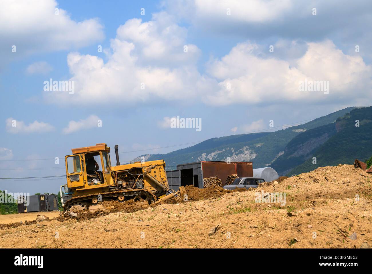 Gelber Bulldozer bewegt Erdreich auf der Baustelle. Bergige Landschaft unter wolkigem Himmel Stockfoto