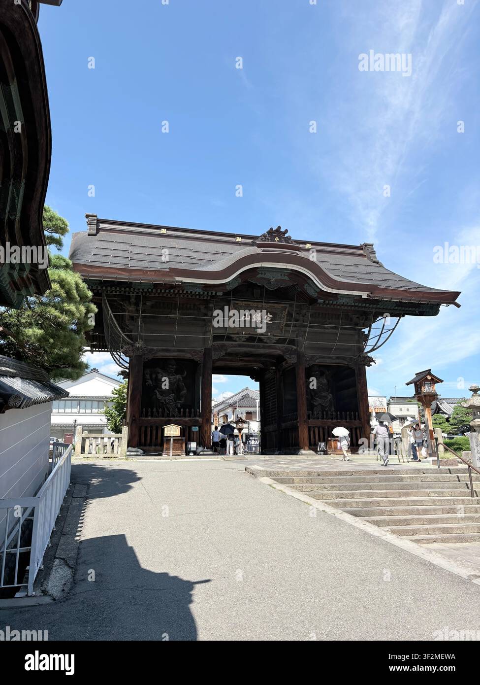 28. August 2025, Nagano, Japan – Monumentales hölzernes Sanmon-Tor des Zenkoji-Buddhistengtempels mit geschnitzten Paneeln und Kanji-Inschrift, blauer Himmel im Hintergrund. - Smartphone-aufgenommenes Stockfoto