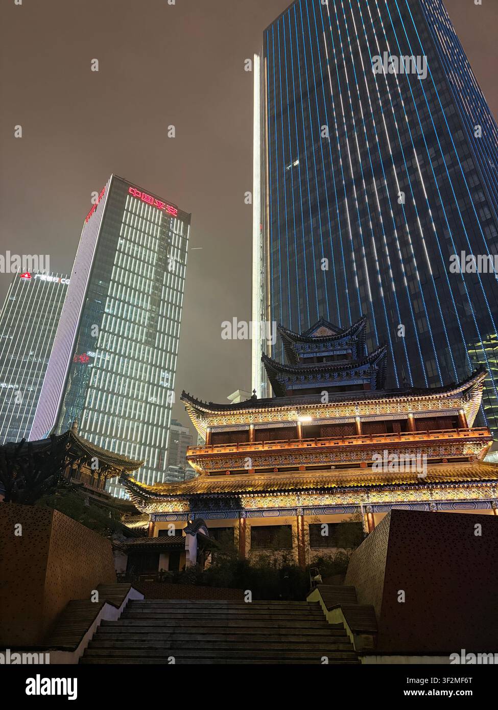 7. November 2025, Chongqing, China – Dramatischer Nachtkontrast zwischen kunstvoll verzierten traditionellen chinesischen Pagodendächern und modernen beleuchteten Glas-Hochhäusern im CBD des Yuzhong-Bezirks. - Smartphone-aufgenommenes Stockfoto